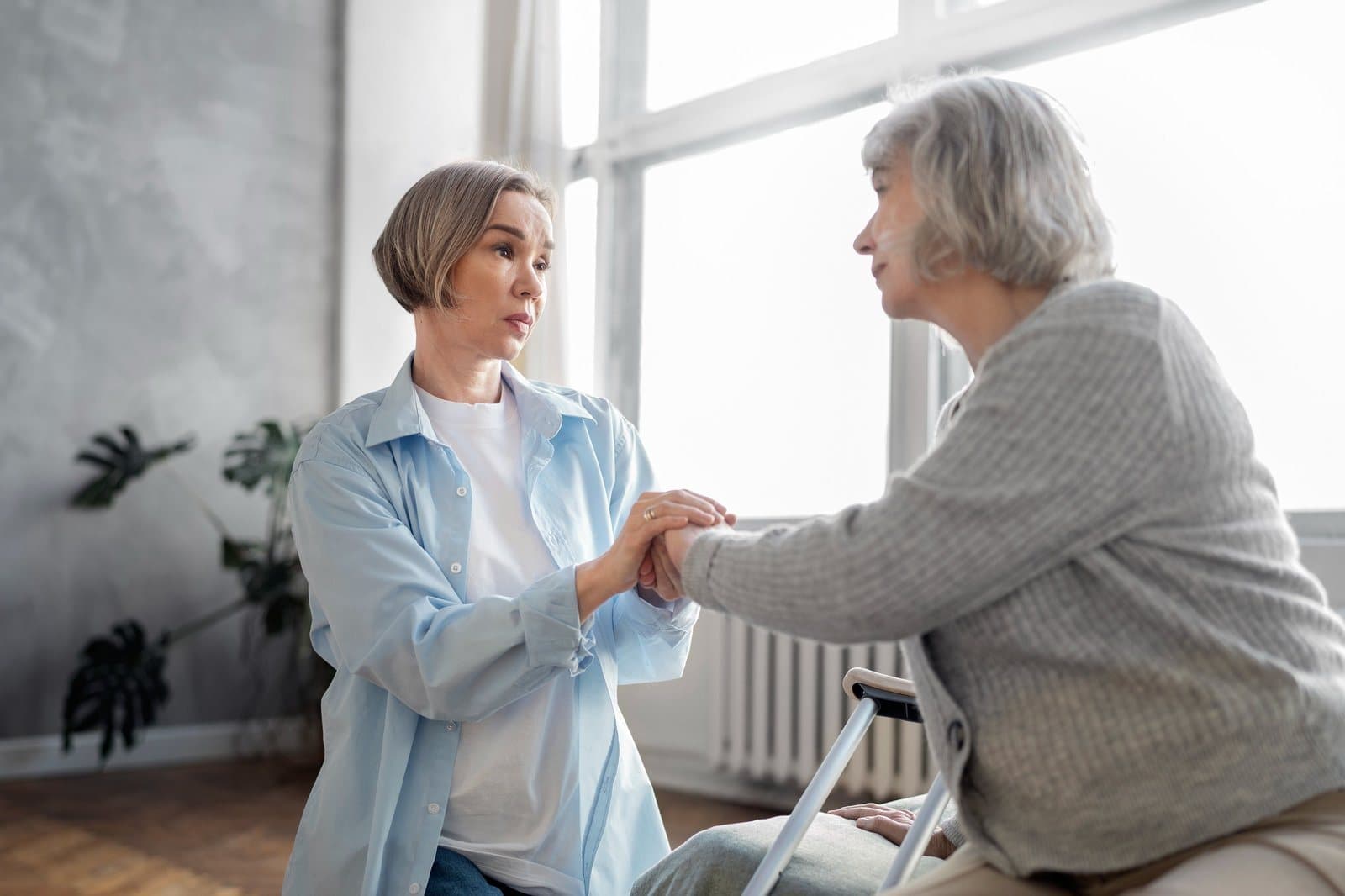 Pflegefachkraft stützt eine Seniorin beim Aufstehen vom Rollator