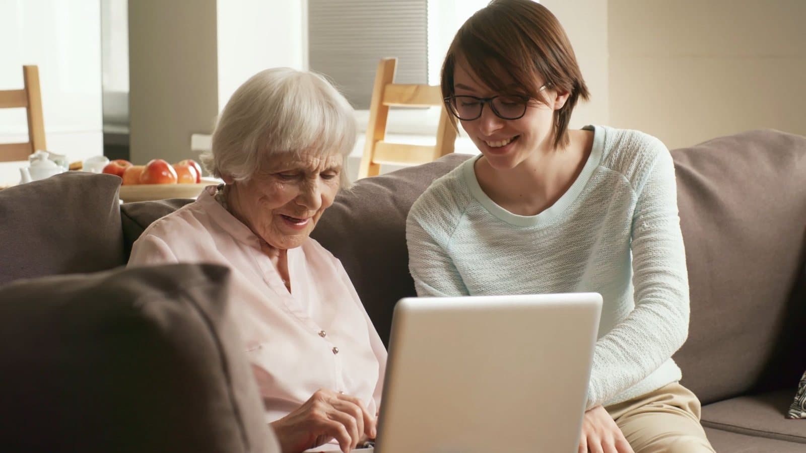 Pflegekraft und Seniorin sitzen gemeinsam am Laptop